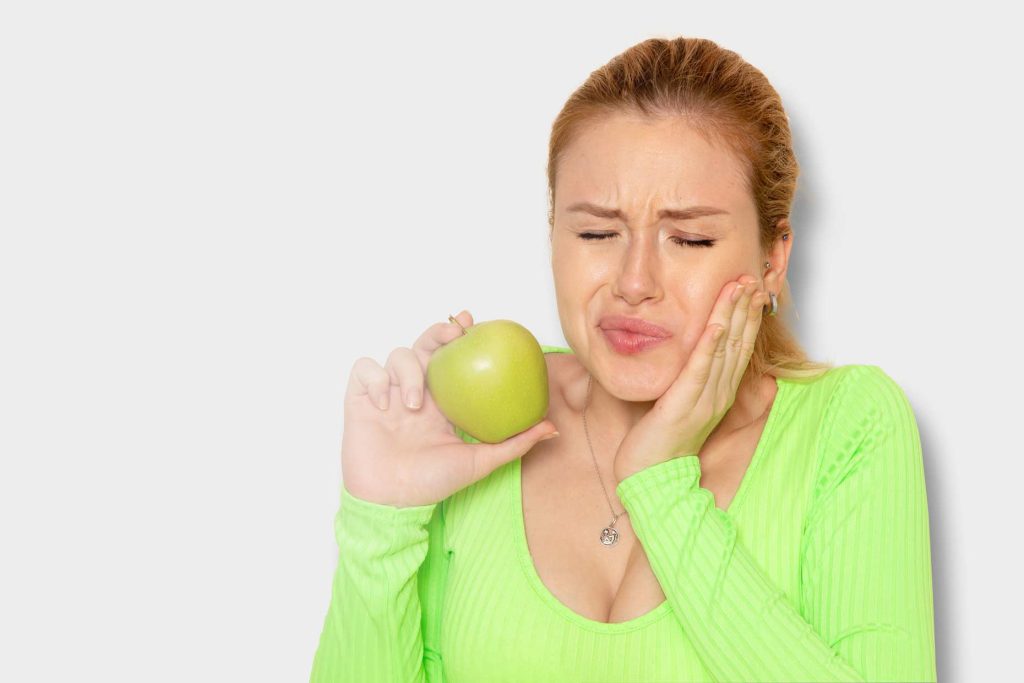 mujer sosteniendo una manzana verde con dolor de dientes por dientes sensibles
