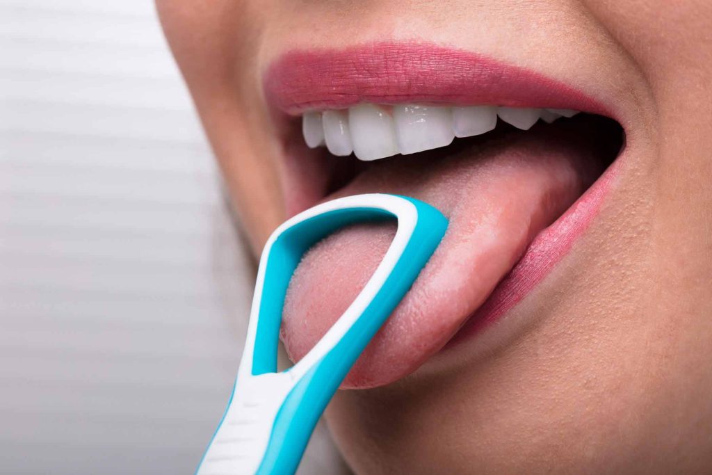 Mujer limpiándose la lengua con un raspador lingual